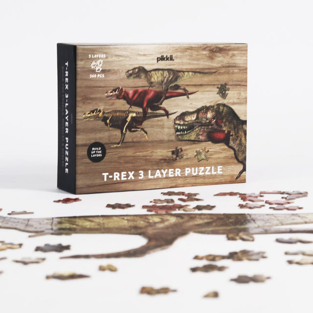T-Rex Layer Jigsaw Puzzle by Pikkii - Front of Packaging on Grey Background Behind Puzzle Pieces