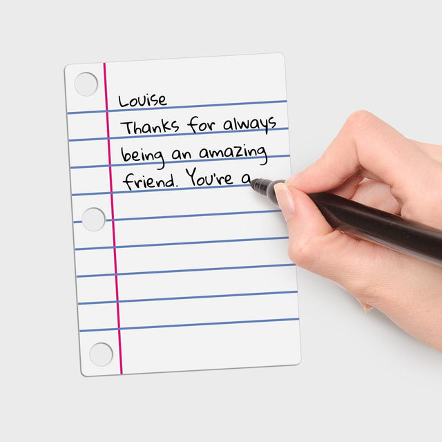 Hand using a black pen to write a personalised message on Pikkii Diy Shrink Little Lined Letter Keychain Canvass over white background