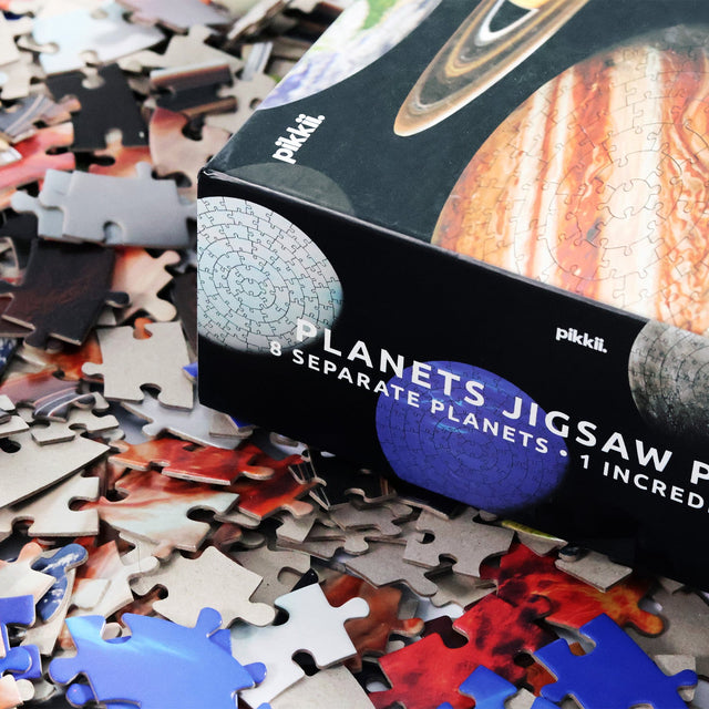 Close up of side of packaging on top of puzzle pieces of Pikkii's planets jigsaw puzzle