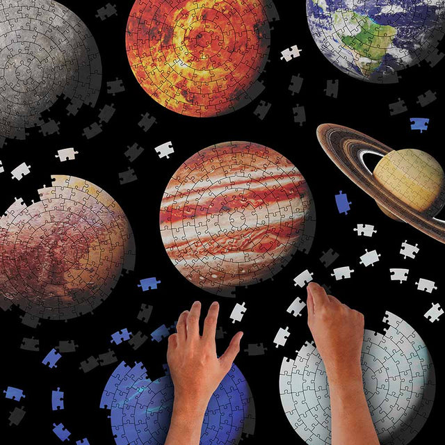 Hands assembling Pikkii Planets Jigsaw Puzzle over Black Background