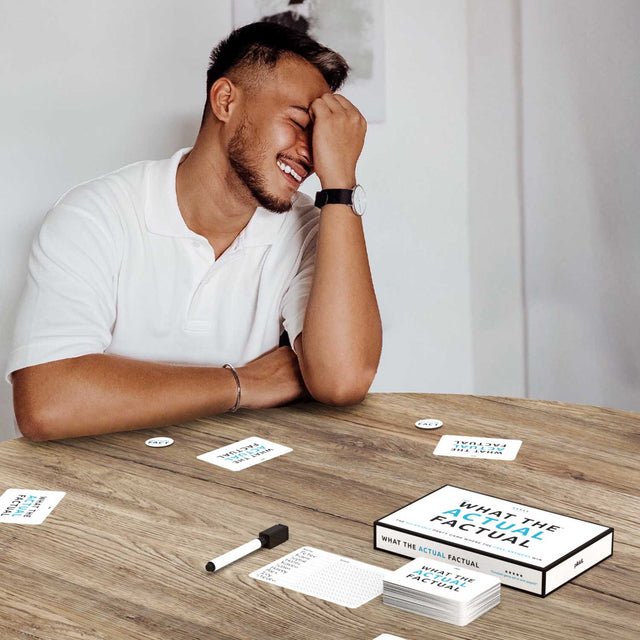 Man Sitting at Table Laughing playing What the Actual Factual Party Game
